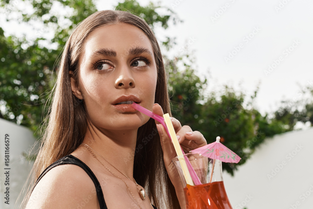 Fototapeta premium Young beautiful woman enjoying a refreshing drink during a sunny summer day outdoors