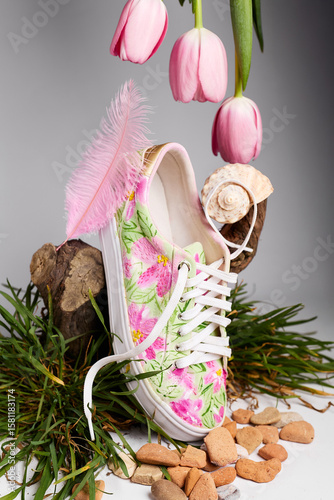 Floral sneaker with pink tulips, feather, seashell, and grass on studio background