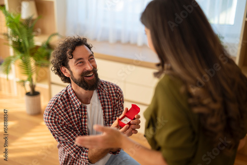 Photos Smiling man proposing to woman with engagement ring box in hand at home