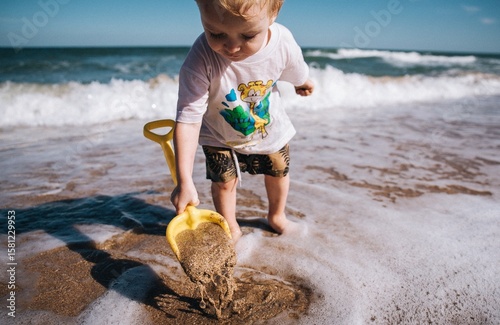 little boy playing digging sand with a shovel at sea