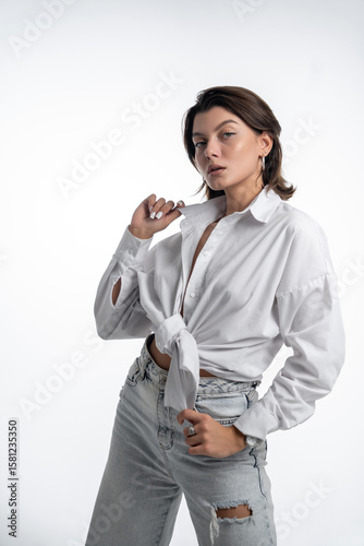 A woman with glasses and ripped jeans poses against a white background