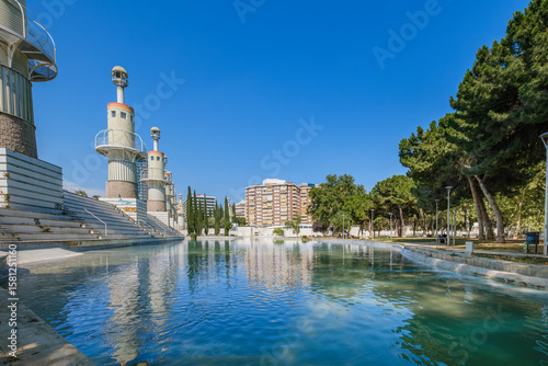Urban Lake With Green Water in Parc Espanya Industrial Barcelona Spain. Public park pond, apartment buildings, cypress trees, recreational area, city landscape