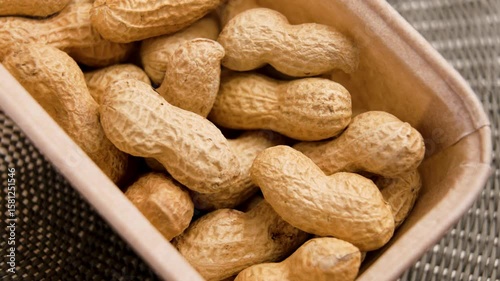 Unshelled roasted peanuts in paper store pack on a wicker mat. Rotation
