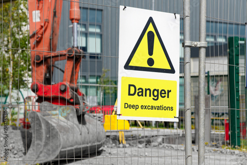 Deep excavations danger sign on fence with digger in background on construction site