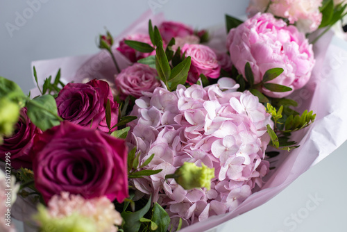 Pink bouquet of roses, peonies, eustoma and hydrangea on a light background. Festive professional flower arrangement in soft pink tissue paper. Romantic bouquet of buds and greenery close-up