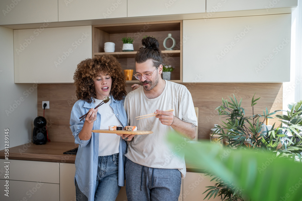 Fototapeta premium Couple eating sushi in modern kitchen using chopsticks