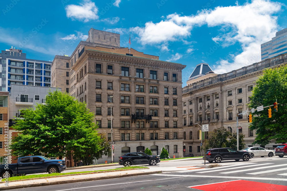 Fototapeta premium A clean, well-structured sidewalk corridor lined with commercial buildings and high-rises under a blue sky.