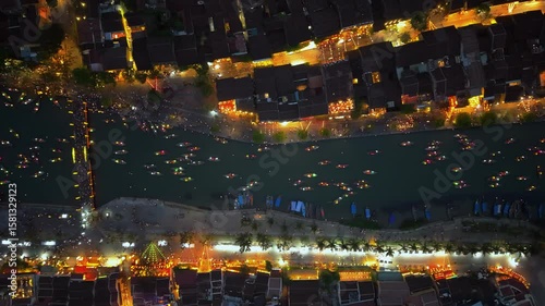 Drone flight over the Thu Bon River in the beautiful Vietnamese city of Hoi An at night. shows small boats on the water, iconic yellow buildings, colorful lanterns, and many people walking.