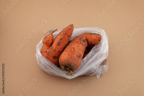 Ugly vegetables. Carrots with flaws in plastic bag on beige background. Concept - Food waste reduction. Using in cooking imperfect products