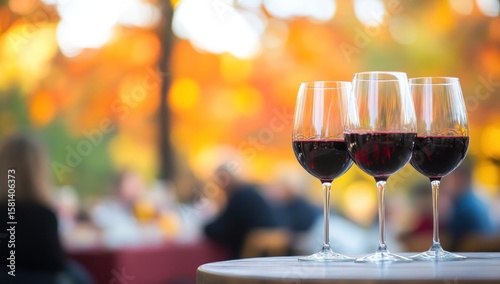Three glasses of red wine on a table outdoors with autumn background.
