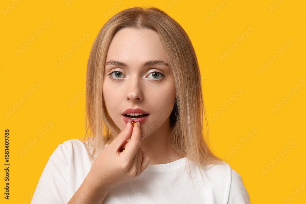Young woman taking vitamin A pill on yellow background, closeup Young woman taking vitamin A pill on yellow background, closeup