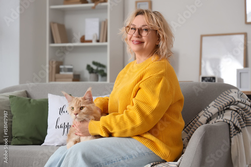 Beautiful middle-aged woman with cute cat sitting on sofa at home