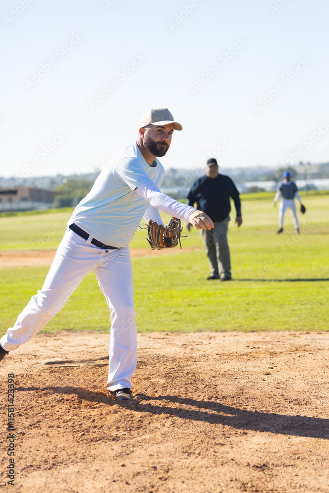 Diverse male teammates pitching from mound and fielding on baseball diamond at community park Diverse male teammates pitching from mound and fielding on baseball diamond at community park