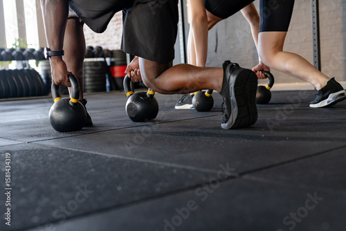 Diverse workout partners performing kettlebell plank on rubber mat floor with squat rack and plates