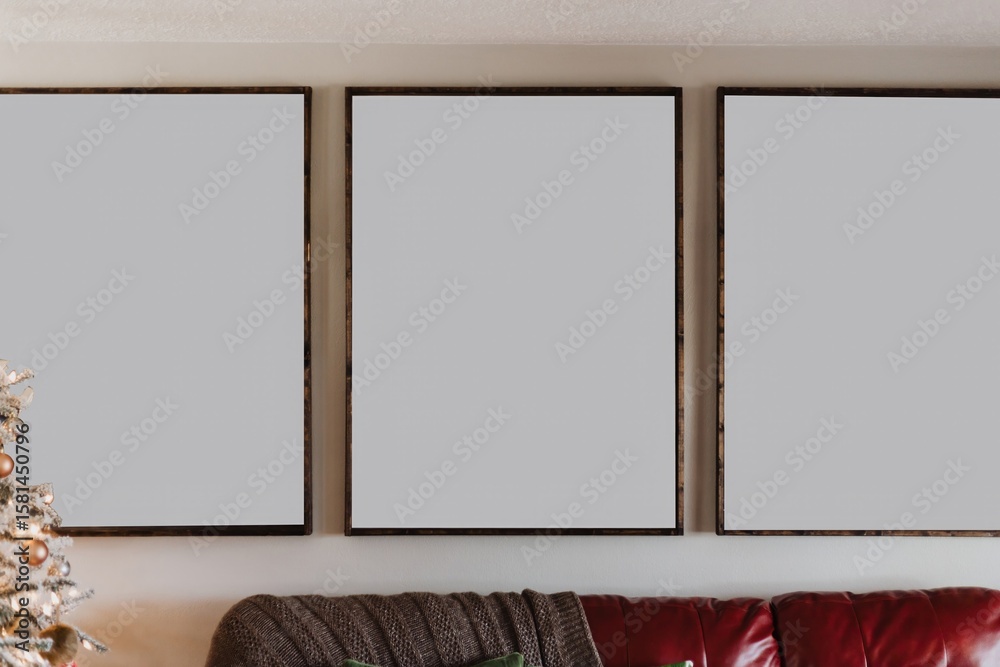 Fototapeta premium Triptych mockup with three blank frames above red leather couch in cozy holiday living room with Christmas tree and neutral modern decor