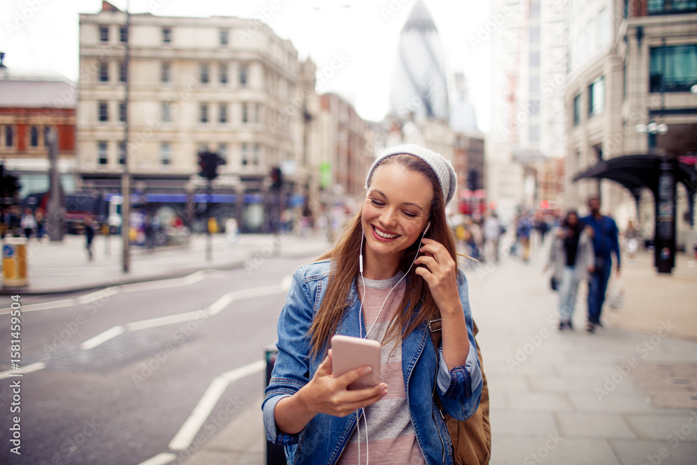 Fototapeta premium Young woman using a smart phone while walking down a sidewalk in London