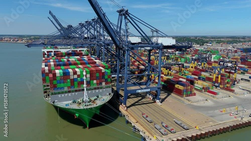 Aerial drone shot Felixstowe busy port cargo ships, shipping containers, huge cranes, loading and unloading heavy goods vehicles summer maritime business England UK.