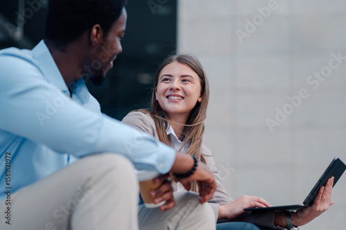 Business colleagues collaborating outdoors using laptop and enjoying coffee break