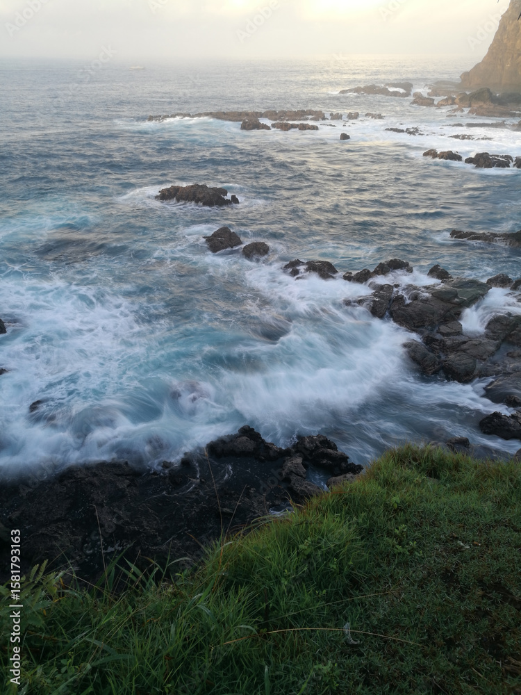 Dramatic ocean view with misty waves and rugged rock formation, the green grass in the foreground gives natural accent to the seascape. Dramatic ocean view with misty waves and rugged rock formation, the green grass in the foreground gives natural accent to the seascape.