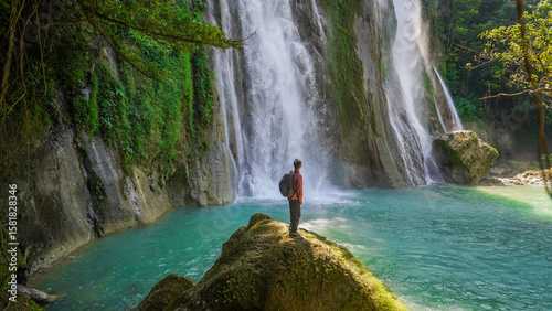 Valokuva Adventurer finds solitude at the base of a roaring waterfall, where blue water m