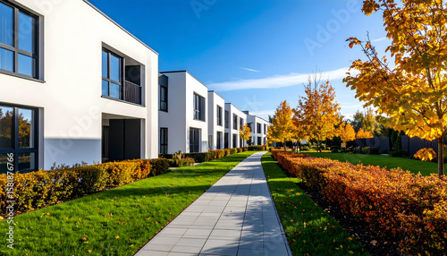 Modern White Residential Buildings with Green Lawns and Vibrant Autumn Trees Under Bright Blue Sky
