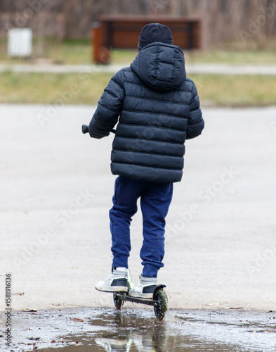 A boy is riding a scooter in the rain