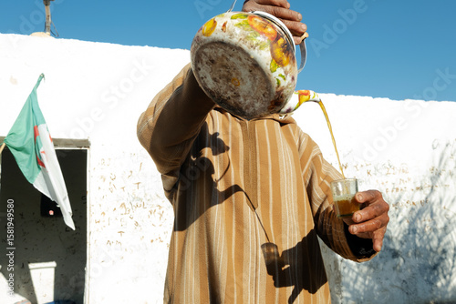 Φωτογραφία Algerian man pouring tea in a glass in front of algerian flag