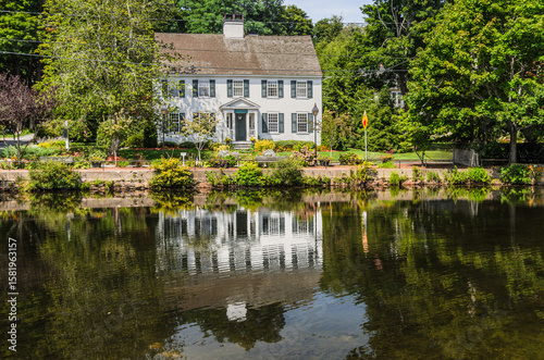 Historic New England house reflected in the calm waters of Shawme Lake, Sandwich, Cape Cod, Massachusetts, USA