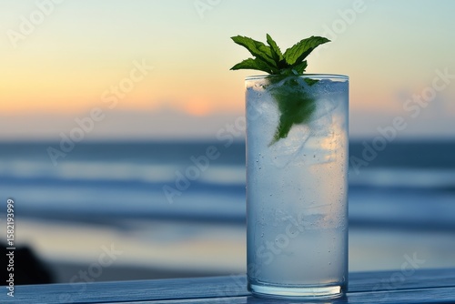 Refreshing drink with mint garnish at sunset overlooking the ocean.