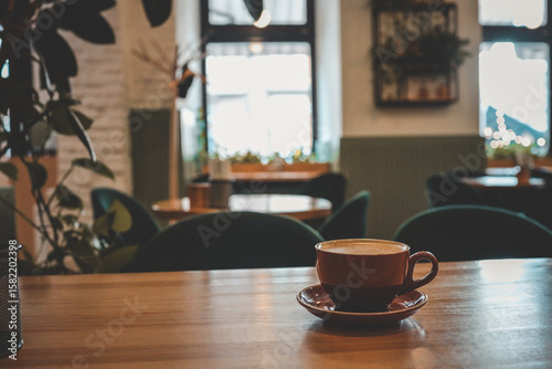 Obraz na plátně Warm and cozy coffee shop interior with a ceramic cup of cappuccino on a wooden