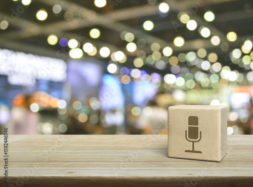 Microphone flat icon on wood block cube on wooden table over blur light and shadow of shopping mall, Business communication concept