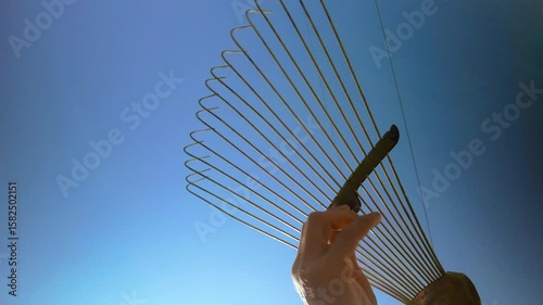 Male hand twisting metal fan rake before cleaning of fallen leaves. Closeup of rake maintenance under bright sky, person tunes tool for landscaping and lawn care