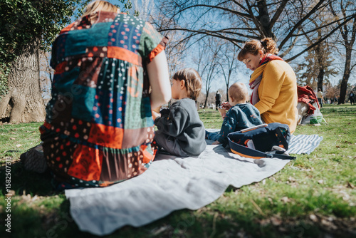 Fotografia A family spends time together sitting on a blanket in a sunlit park, with nature and trees around, enjoying a peaceful outdoor moment