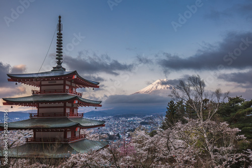 Stunning view of Mount Fuji from Chureito Pagoda in Japan.  Cherry blossoms in full bloom frame the iconic volcano, creating a breathtaking springtime scene. The tranquil cityscape adds depth to this