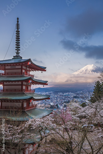 Stunning view of Mount Fuji from Chureito Pagoda in Japan during cherry blossom season.  The iconic red pagoda and pink blossoms create a picturesque scene against the majestic backdrop of Fuji.