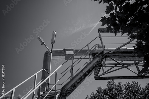 Industrial staircase leads to the sky above a tree line on a bright day, showcasing a blend of nature and urban structures