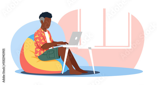 A young man is comfortably working on his laptop while sitting on a beanbag chair near a window, showcasing a modern and relaxed work environment for a company.