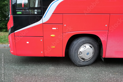 Part of the cabin and a wheel of a red passenger bus on a road.