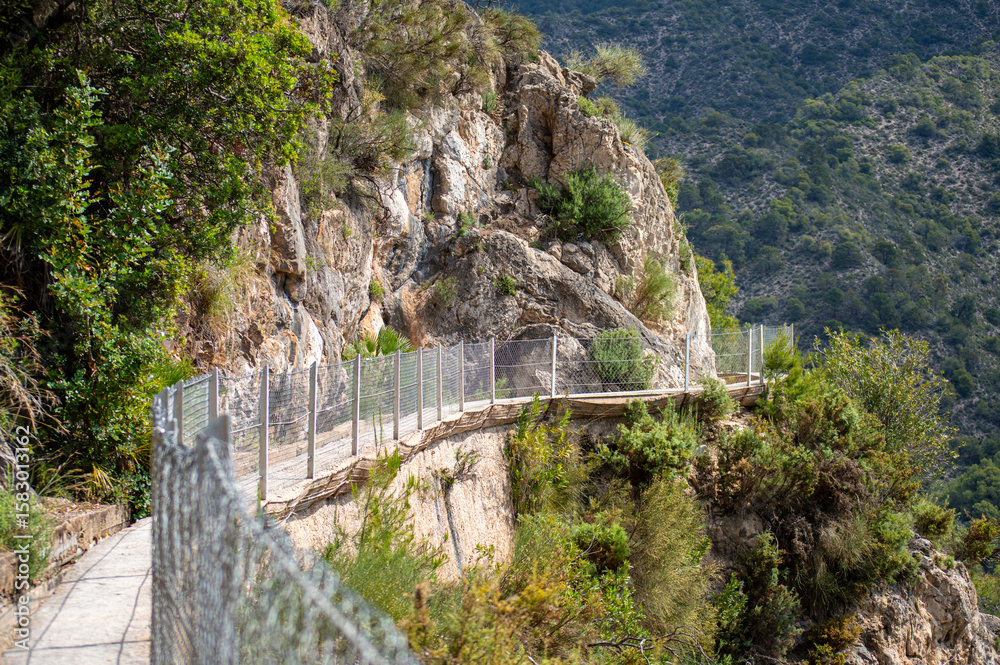 Fototapeta premium Scenic view of surrounding mountains and picturesque village from a hiking trail along an old irrigation ditch in Frigiliana, Spain.