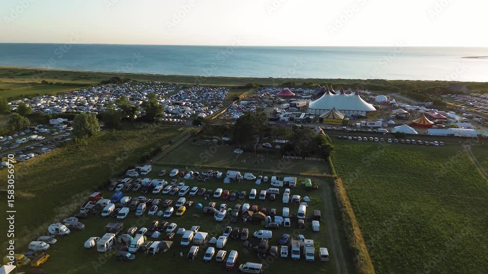 Drone footage reveals the expansive camping grounds of the Chauffer dans la noirceur festival in Normandy, illuminated by the warm tones of sunset.