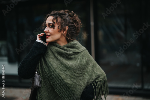 Fototapeta Stylish woman wrapped in a green shawl speaking on her mobile phone in the city