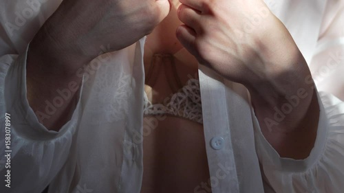 Woman unbuttoning white shirt revealing belly piercing and lace bra