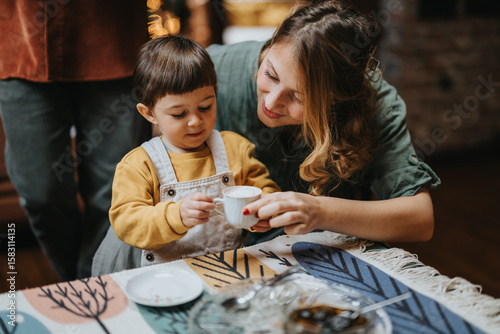 Canvas Print A caring mother engages with her young child, guiding them in a cozy and warm home environment