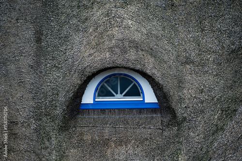 A round window in the roof of a thatched roof house in Germany.