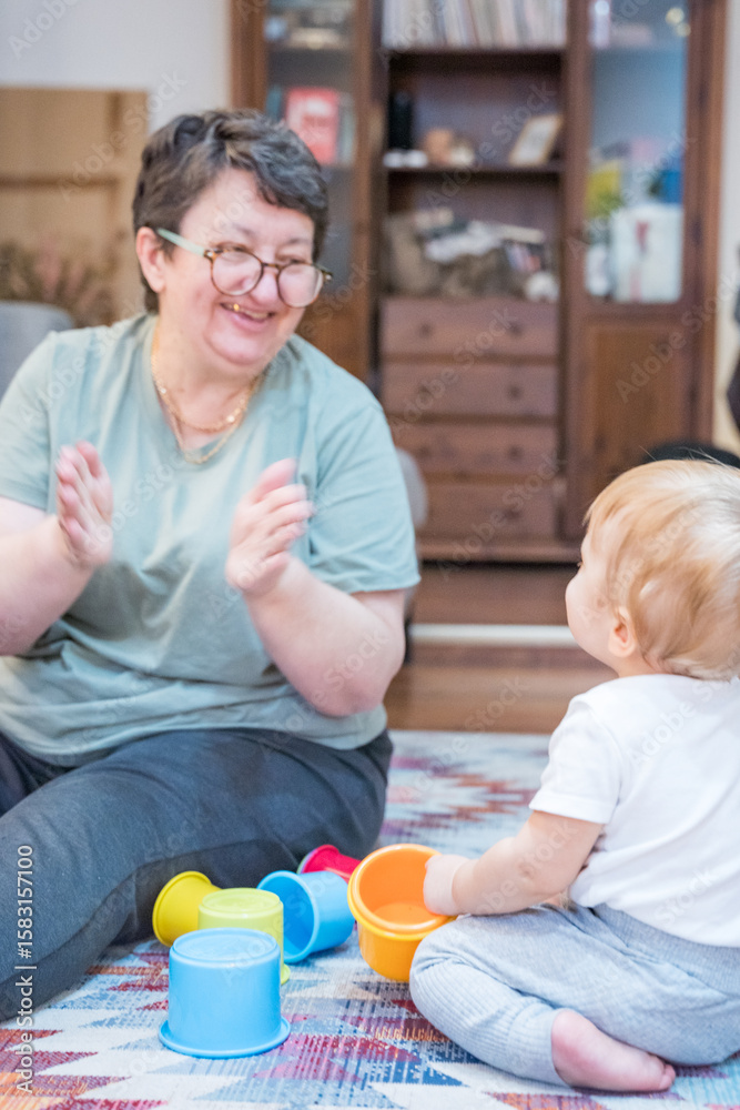 Grandmother clapping while playing with baby and colorful cups on carpeted floor Grandmother clapping while playing with baby and colorful cups on carpeted floor