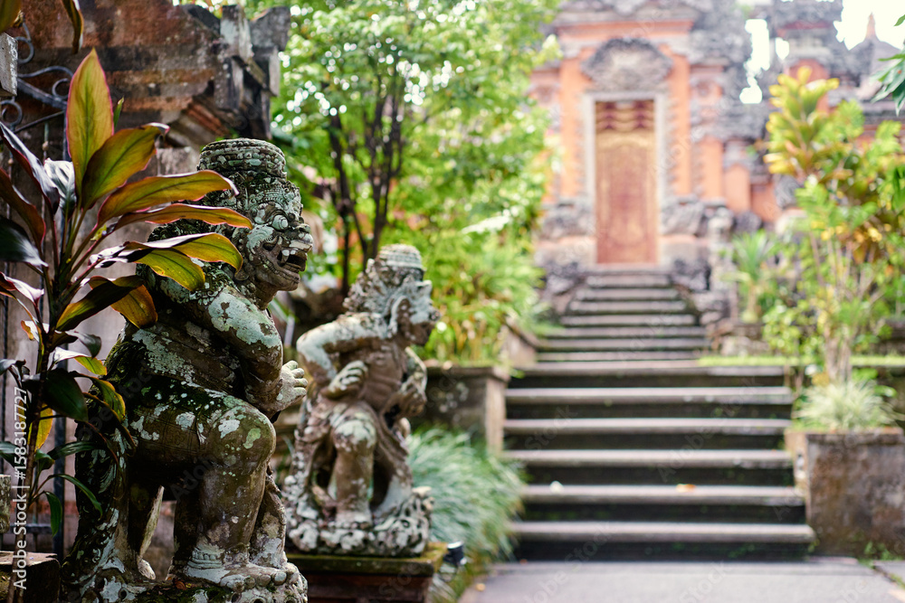 Fototapeta premium Intricate Balinese Stone Statues at Temple Entrance Surrounded by Lush Greenery