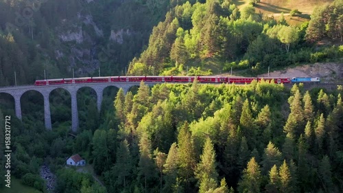  Passenger train crossing the Landwasser Viaduct in the Swiss Alps, red train on the railway. Unesco World Heritage, Red train on famous bridge.The Rhaetian Railway section from the Bernina area