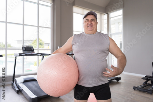 Portrait of mature male standing and holding ball for doing cardio workout in gym club. Fitness, gym and exercising
