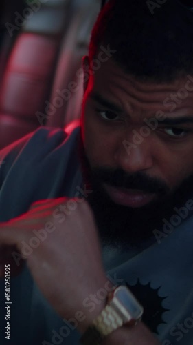 Man sits on driver seat of car illuminated by red and blue light