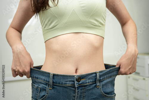 Young Asian woman losing weight wearing loose pants in oversize jeans.